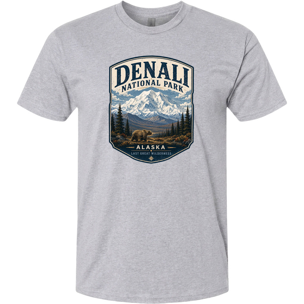 A gray t-shirt with a graphic design depicting a mountain landscape with a bear in the foreground, surrounded by pine trees and mountains.