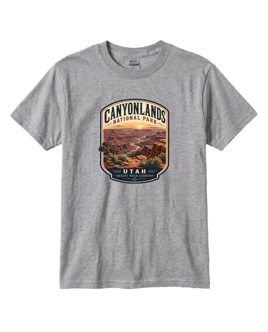 A gray t-shirt with a graphic design depicting a scenic landscape, including mountains, a river, and a sunset. The text on the design reads "CANYONLANDS NATIONAL PARK UTAH DESERT MESA COUNTY".