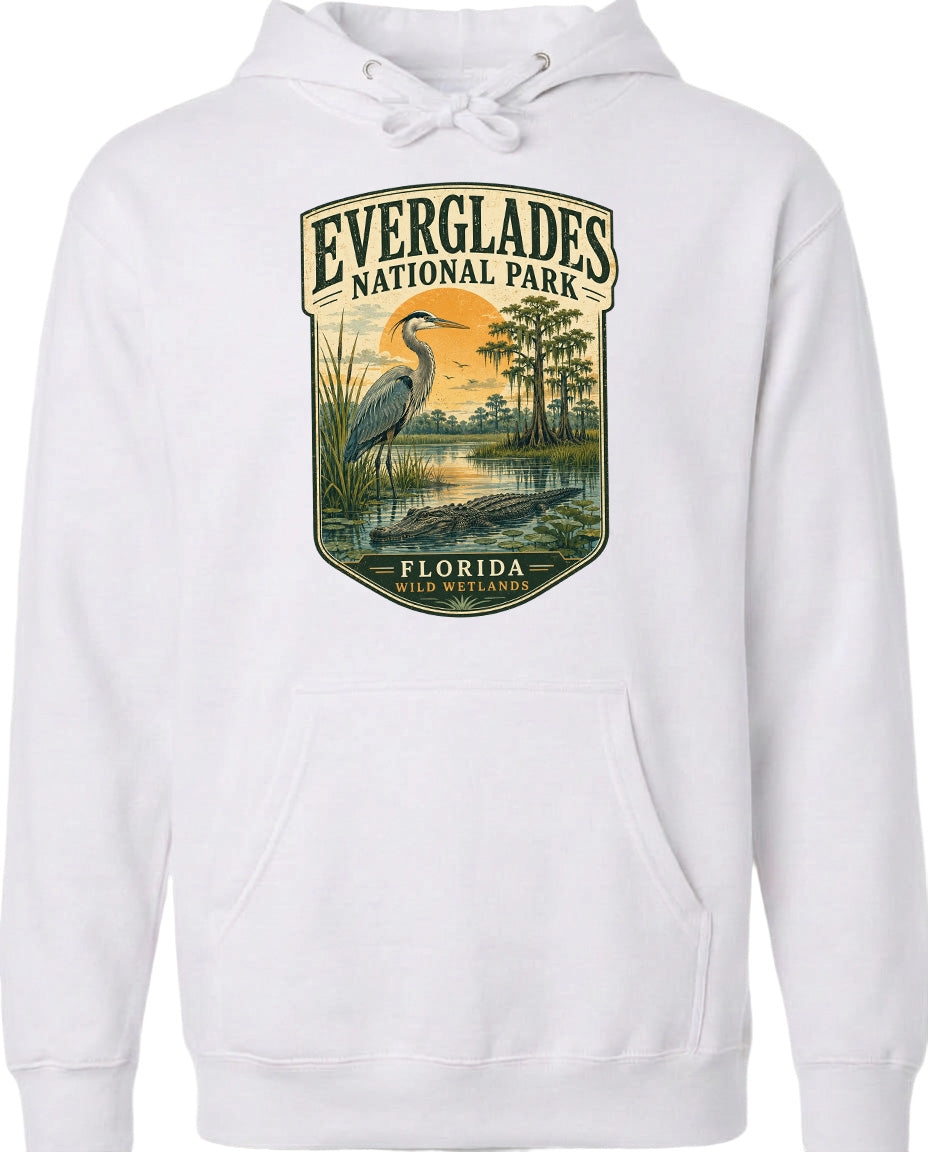 A white hoodie with a graphic design depicting a bird standing in a marshy area with trees and a sunset in the background.