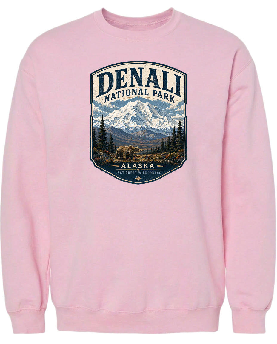 A pink sweatshirt with a graphic design depicting Denali National Park in Alaska, featuring a mountain landscape with a bear in the foreground.