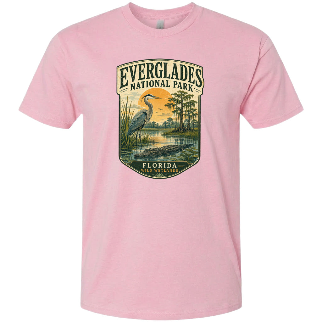 A pink t-shirt with a graphic design depicting a bird, a water feature, and a landscape with trees and a body of water.