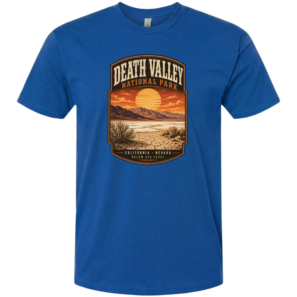A blue t-shirt with a graphic design depicting a desert landscape with mountains, a sunset, and a desert plant.