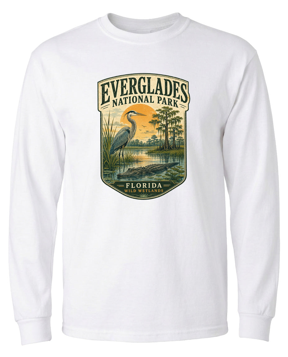 A white long-sleeved t-shirt with a graphic design depicting a bird, likely a heron, standing in a marshy area with trees and a sunset in the background.