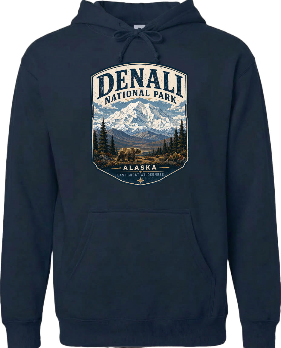 A hoodie with a graphic design featuring a mountain landscape with a bear in the foreground, surrounded by pine trees and mountains.