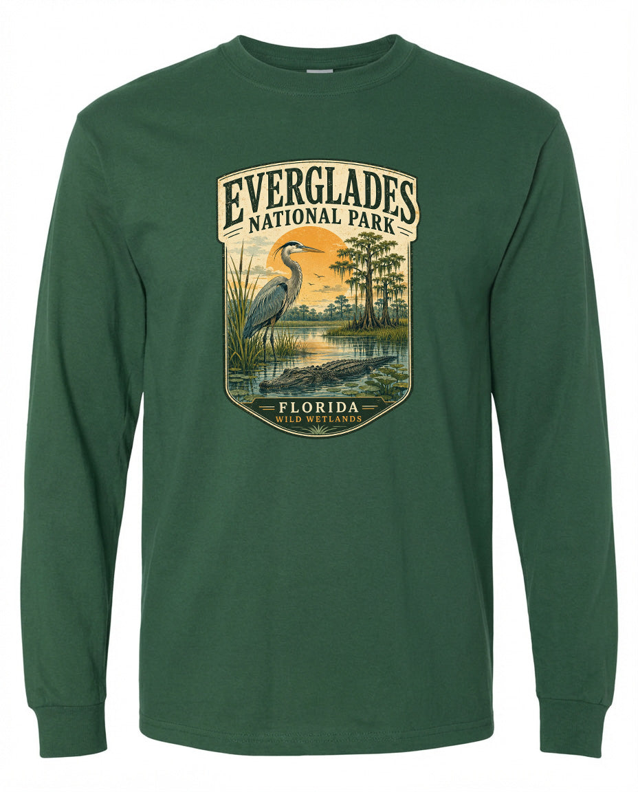 A green long-sleeved t-shirt with a graphic design depicting a bird, a pond, and trees, along with the text "EVERGLADES NATIONAL PARK FLORIDA WILD WETLANDS".