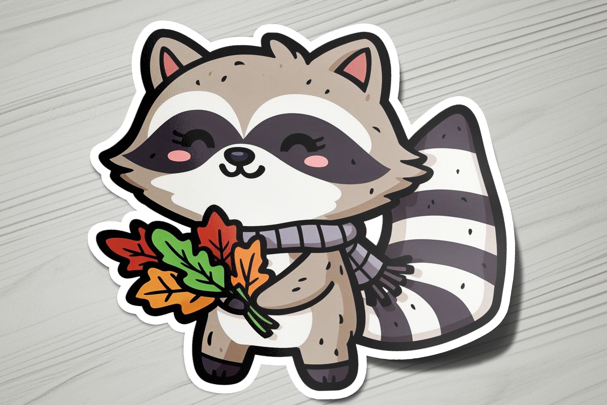 a sticker of a raccoon holding an autumn leaf