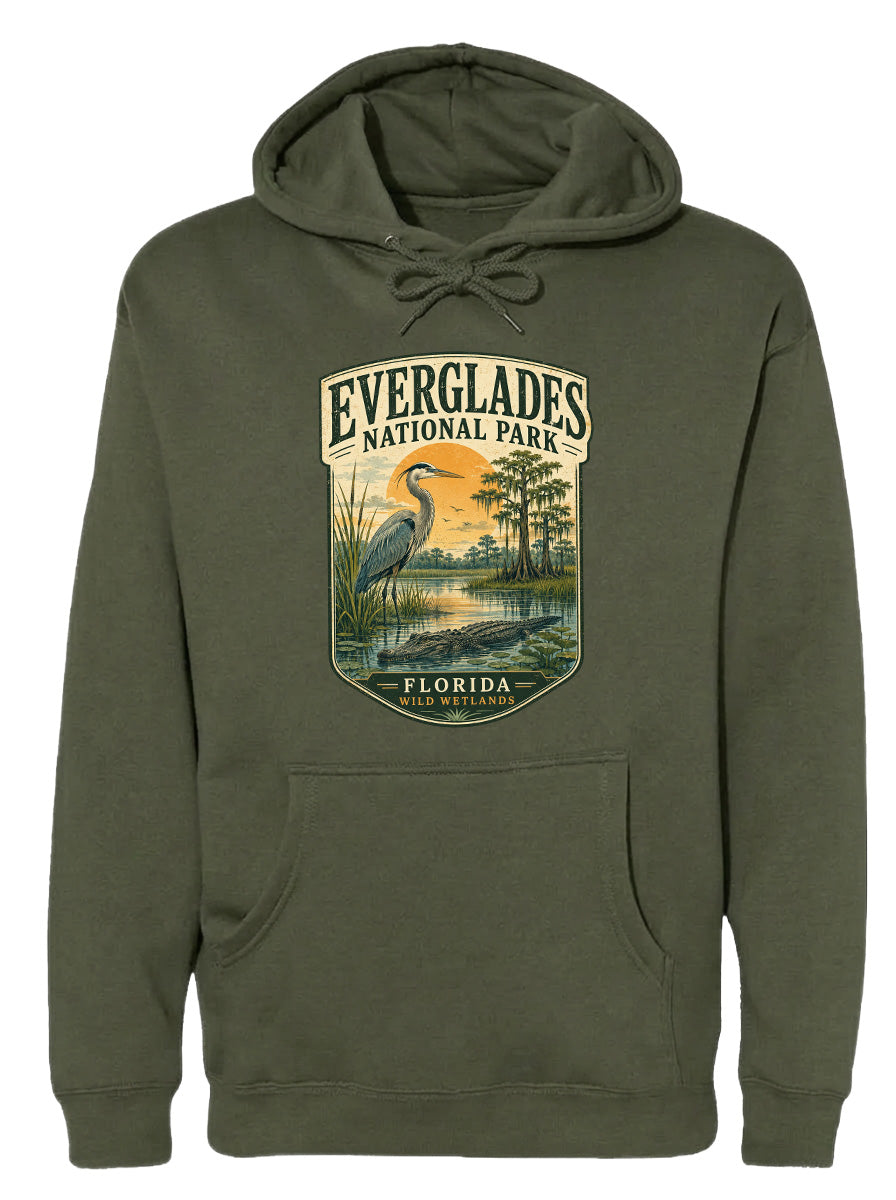 A green hoodie with a graphic design depicting a bird, likely a heron, standing in a marshy area with trees and a sunset in the background.