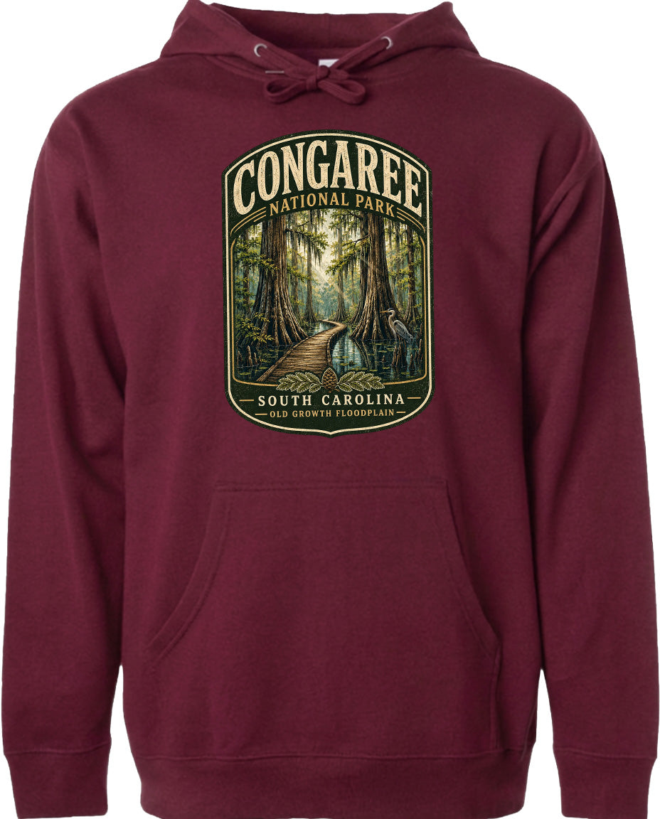 A maroon hoodie with a graphic design depicting a forest scene, including a path leading through the trees and a bird in flight.