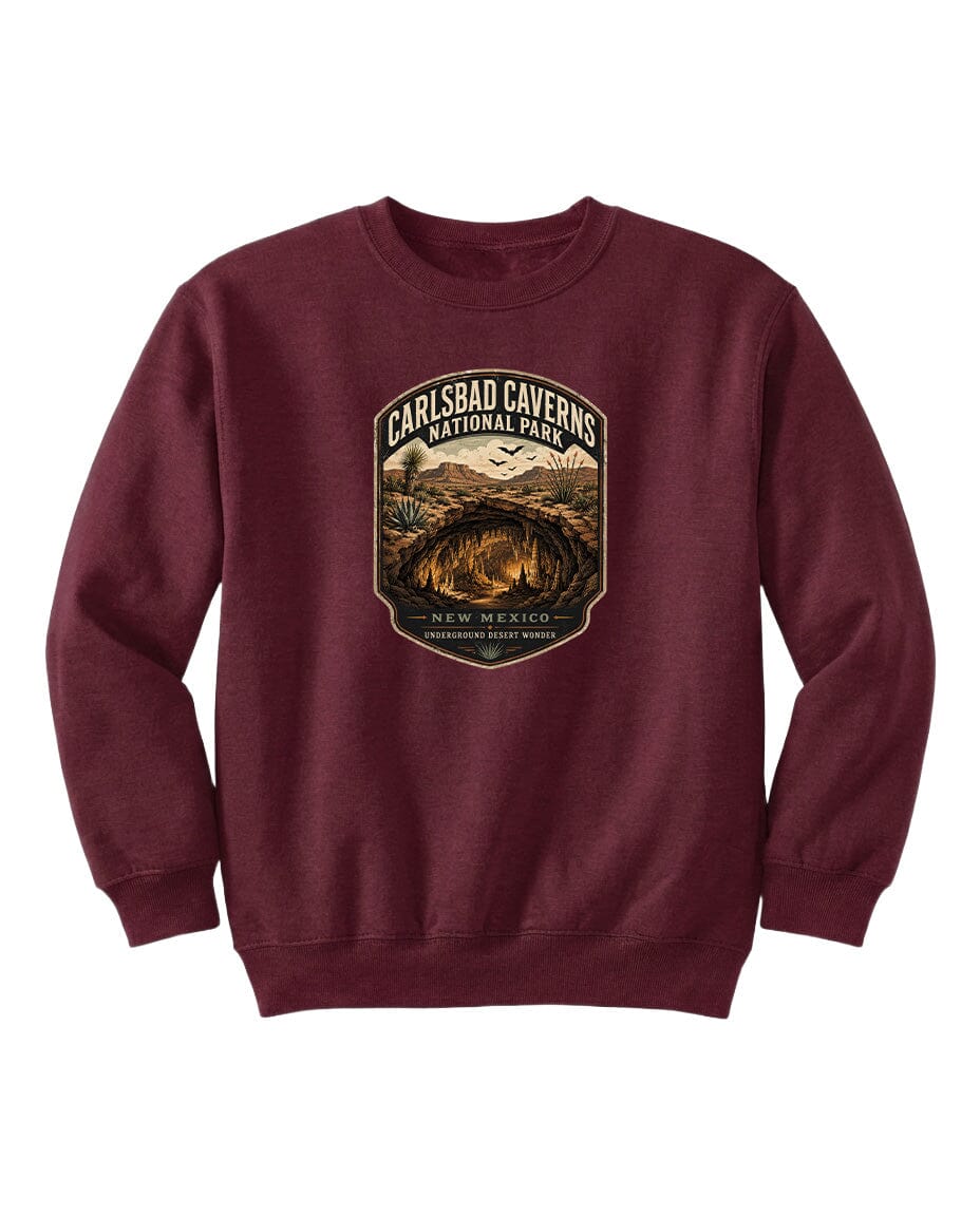A burgundy-colored sweatshirt with a graphic design featuring a shield-shaped emblem that says "CARLSBAD CAVENS NATIONAL PARK" and includes a desert landscape with mountains in the background.