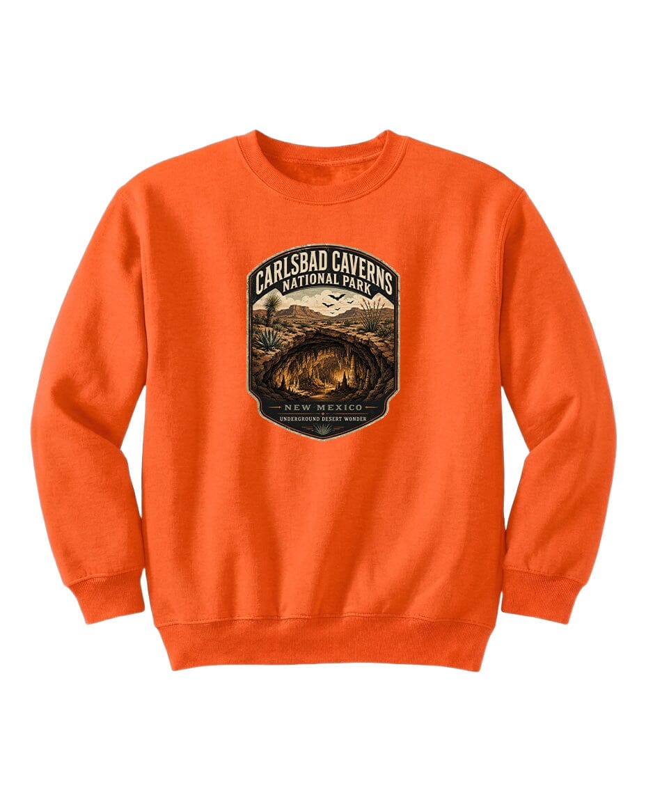 An orange sweatshirt with a graphic design featuring a cave and mountains, along with the text "CARLSBAD CAVENS NATIONAL PARK" and "NEW MEXICO UNDERGROUND WONDER".