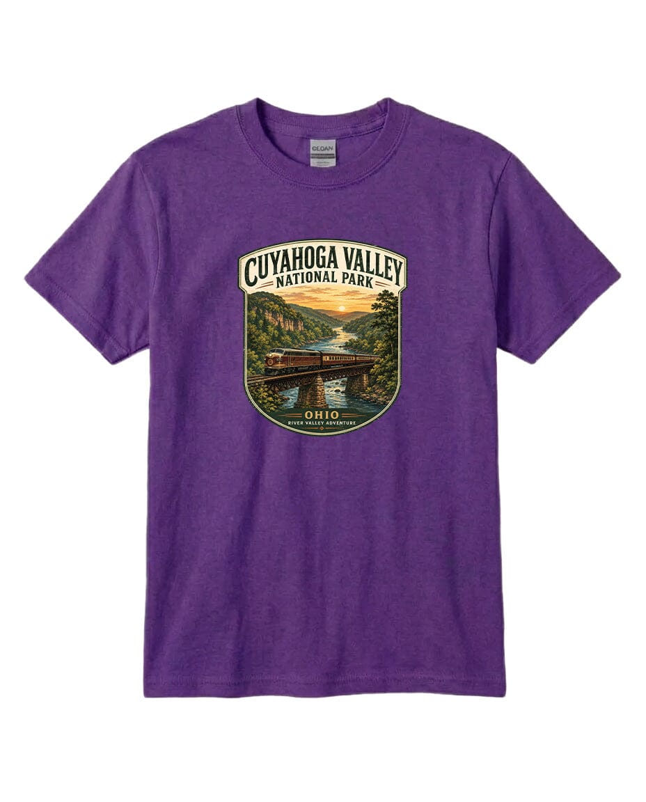 A purple t-shirt with a graphic design depicting a scenic view of the Cuyaños Valley National Park, featuring a bridge, river, and sunset.
